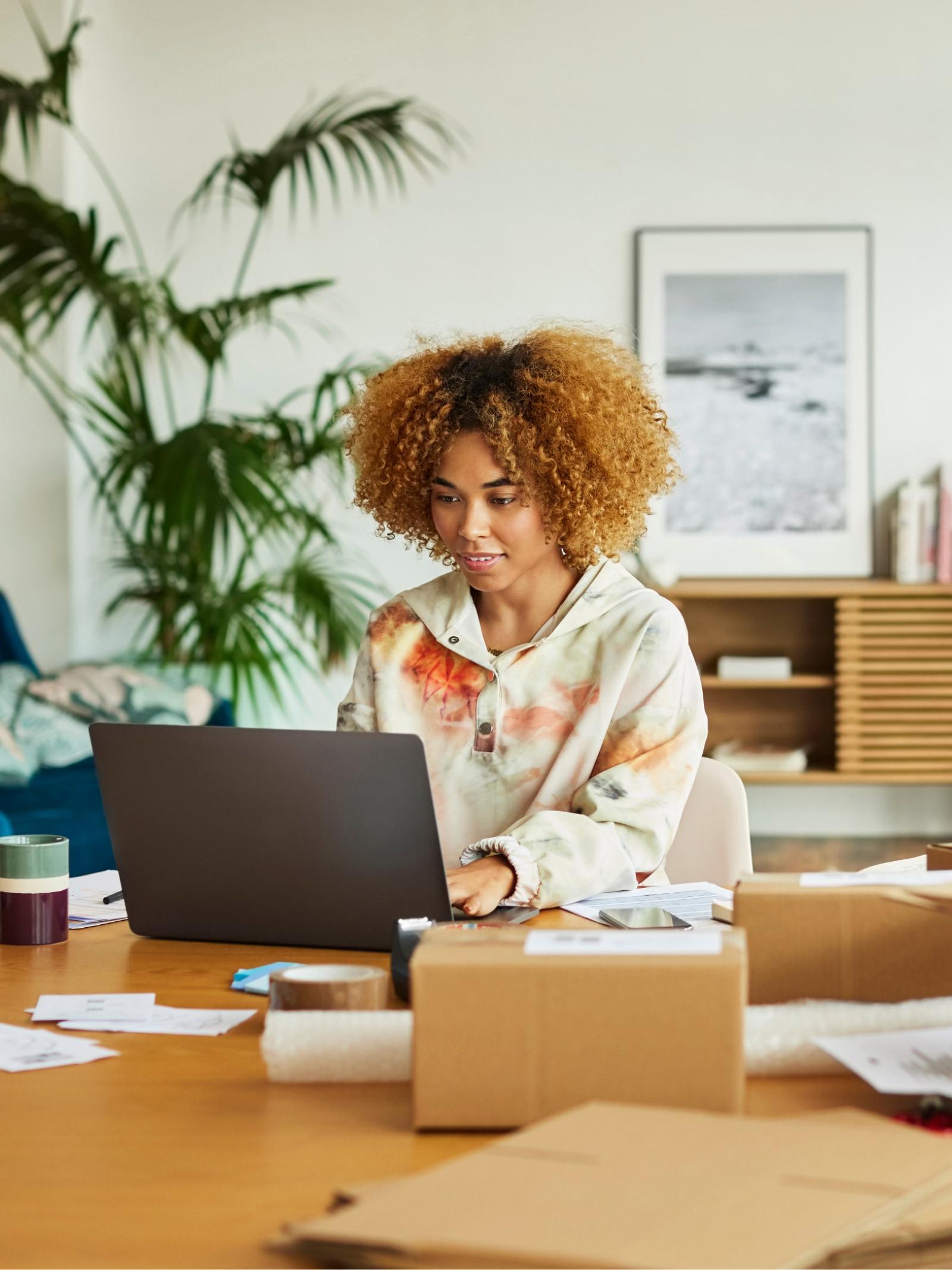 Osoba pracująca na laptopie otoczona kartonowymi pudłami.