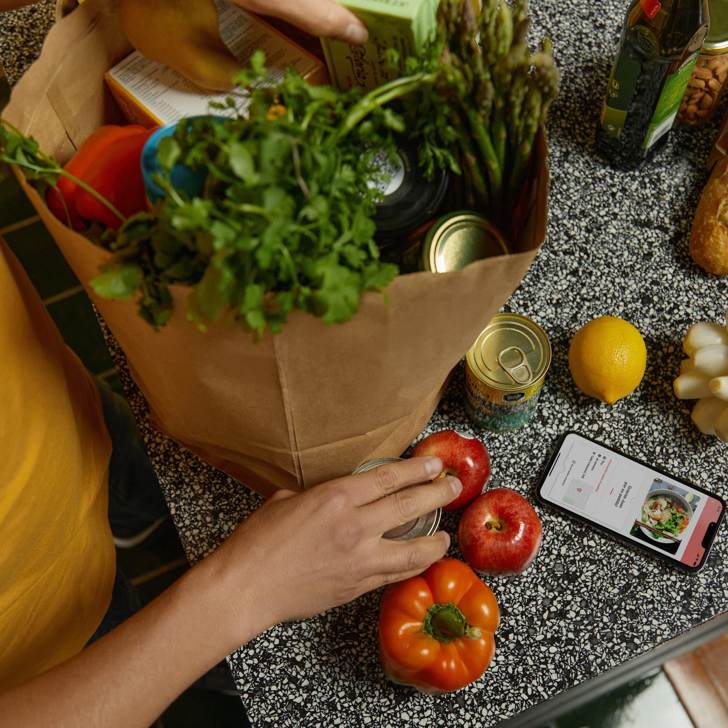 Person som packar upp varor bredvid en smartphone som visar en betalningsapp.