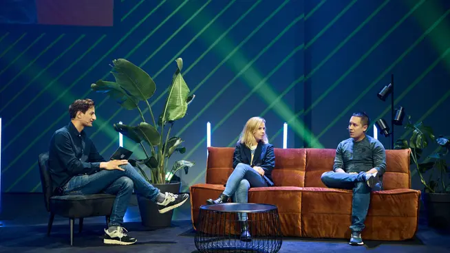 Three people seated on stage involved in a discussion at a corporate event.