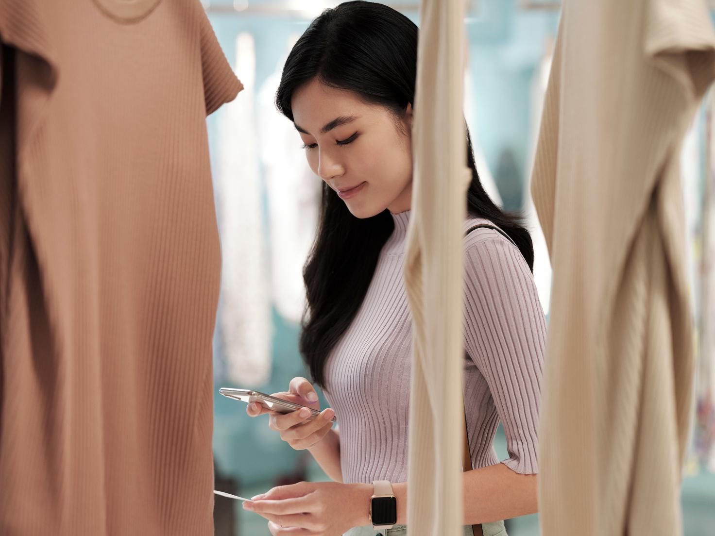 A woman using a phone in a clothing store