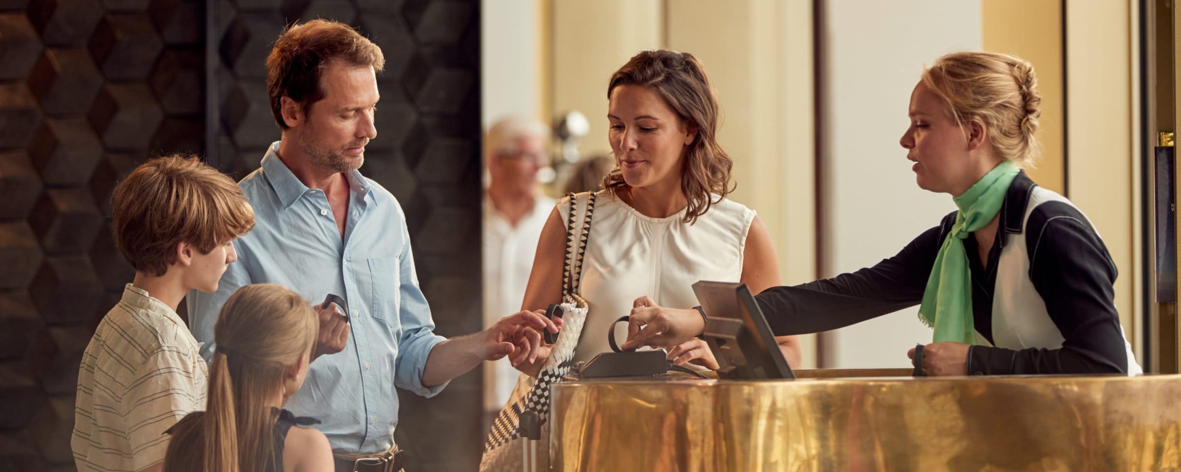 Familia registrando en el mostrador de recepción de un hotel con un miembro del personal asistiendo.