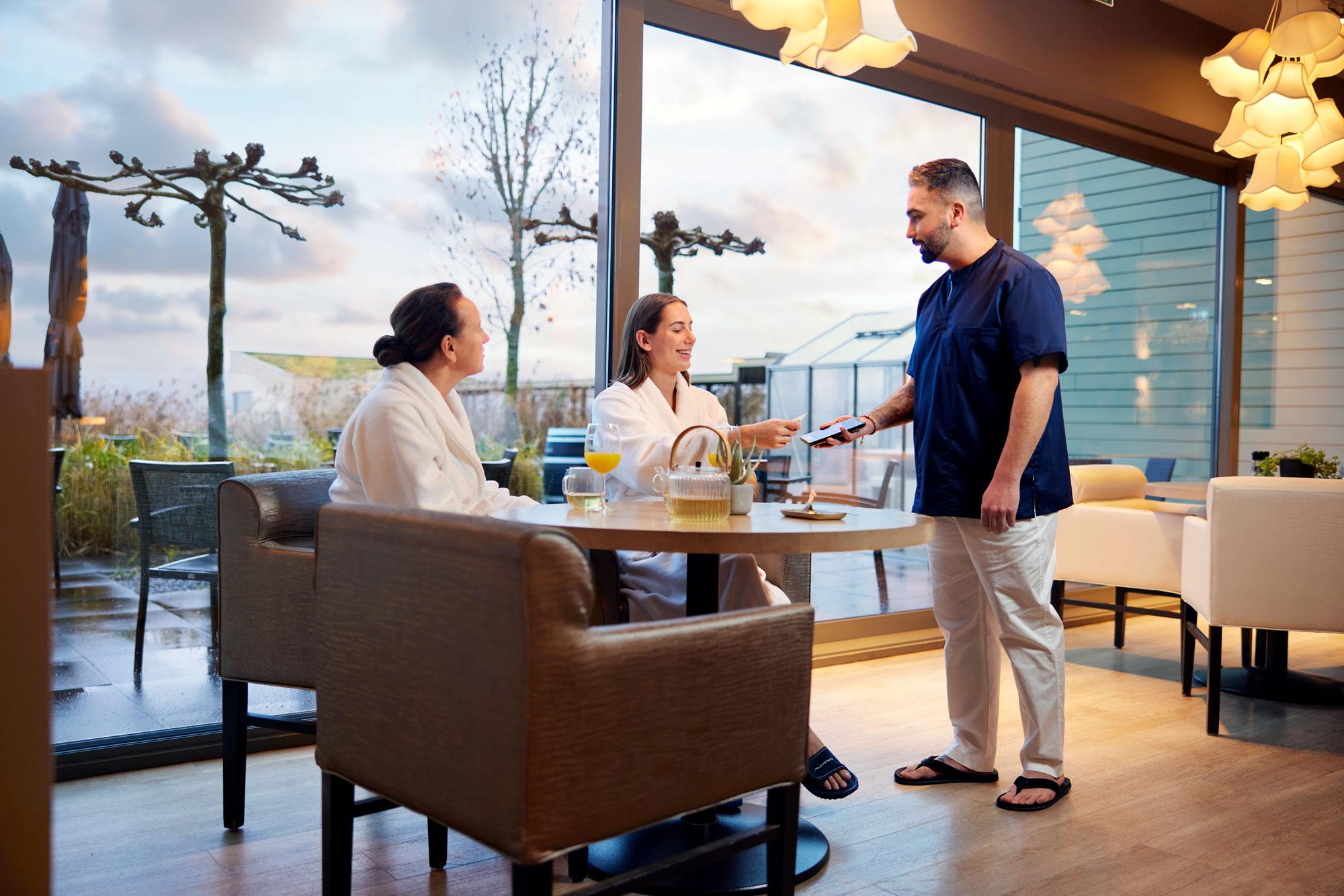 Two women at a table paying for spa and wellness by tapping their card at Adyen's S1E terminal.