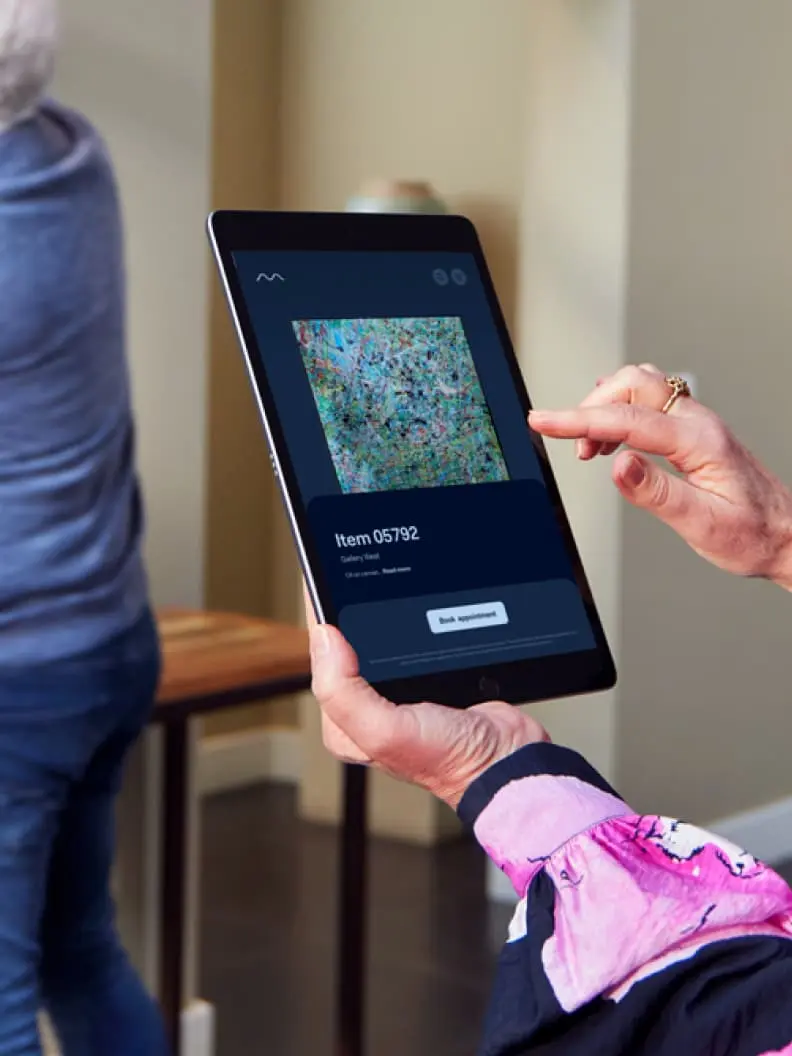Dvě osoby používají tablet k prohlížení položek galerie, pravděpodobně zobrazujících rozhraní Adyen checkout.