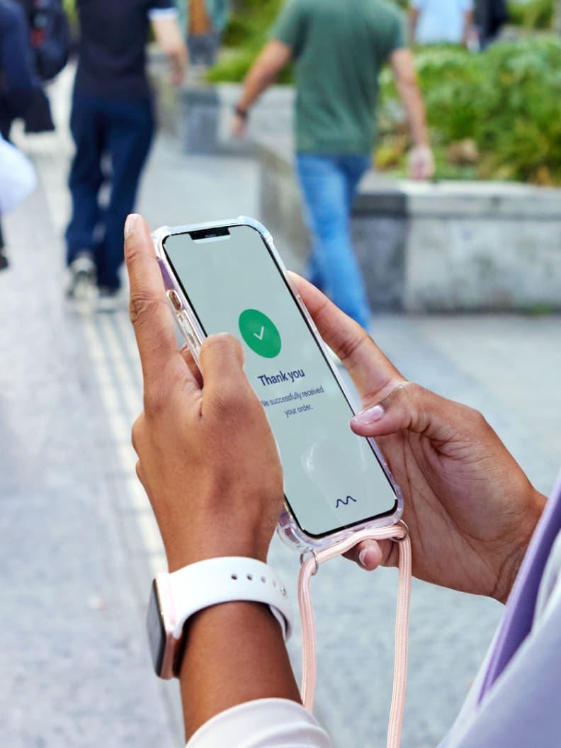 Gros plan des mains d'une personne tenant un smartphone avec un message de 'Merci' et le logo Adyen sur l'écran.