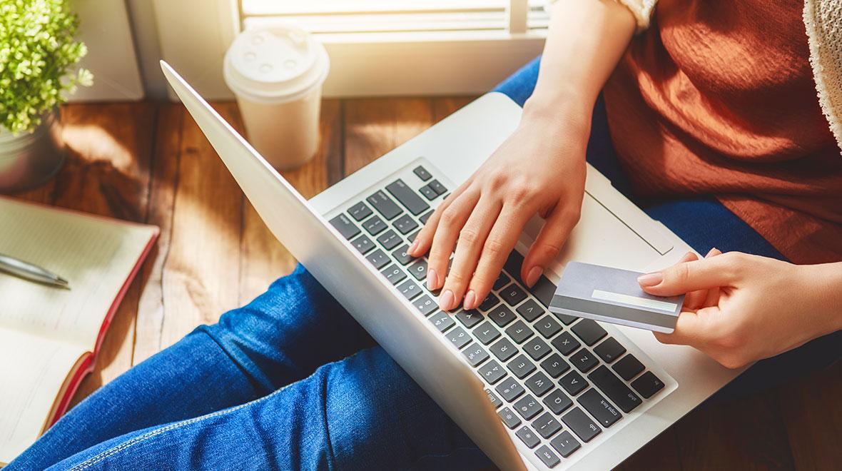 Pessoa segurando um cartão de crédito enquanto usa um laptop para uma compra online