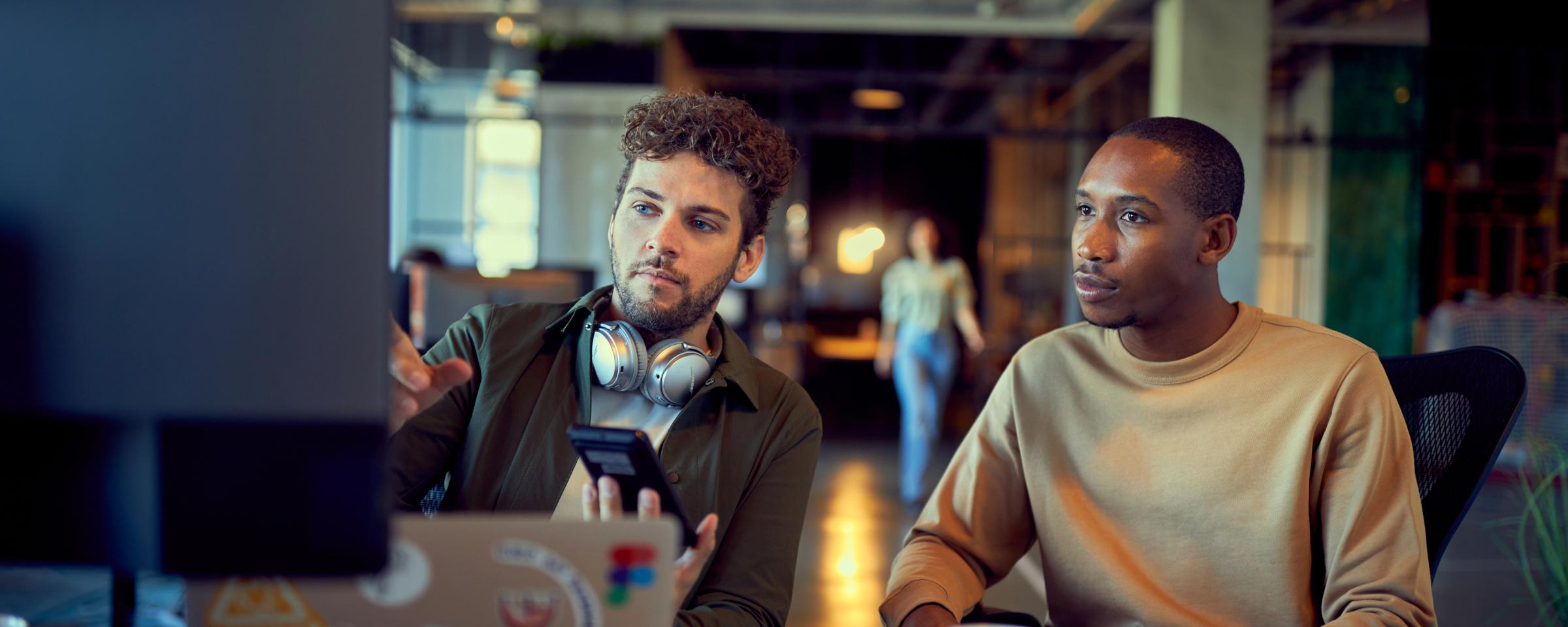 Due professionisti che discutono su uno smartphone accanto a un portatile con adesivi.