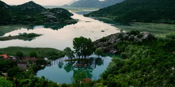 Vista serena del lago con vegetación y un pequeño asentamiento.