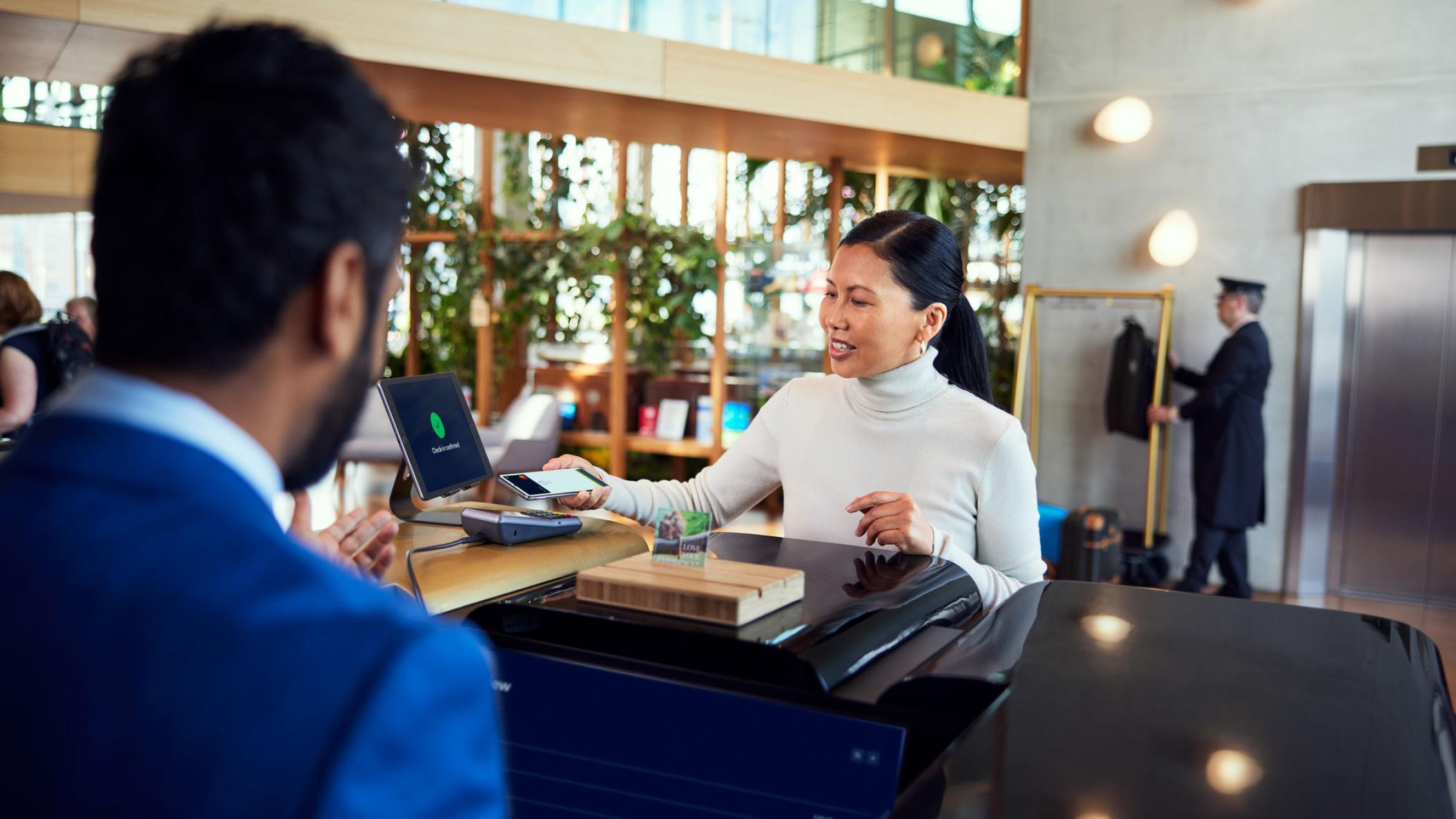 Persona que utiliza un smartphone para realizar un pago en un terminal Adyen en la recepción de un hotel.