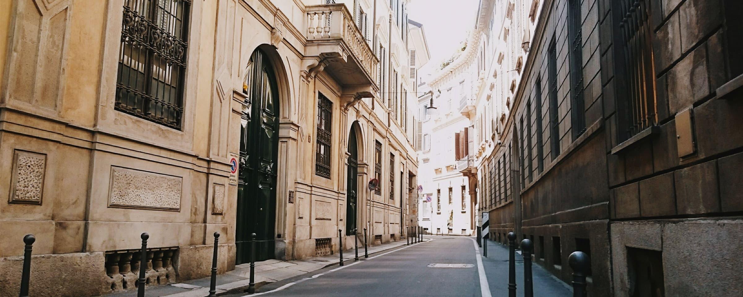 Deserted narrow street with traditional European architecture and parked vehicles.