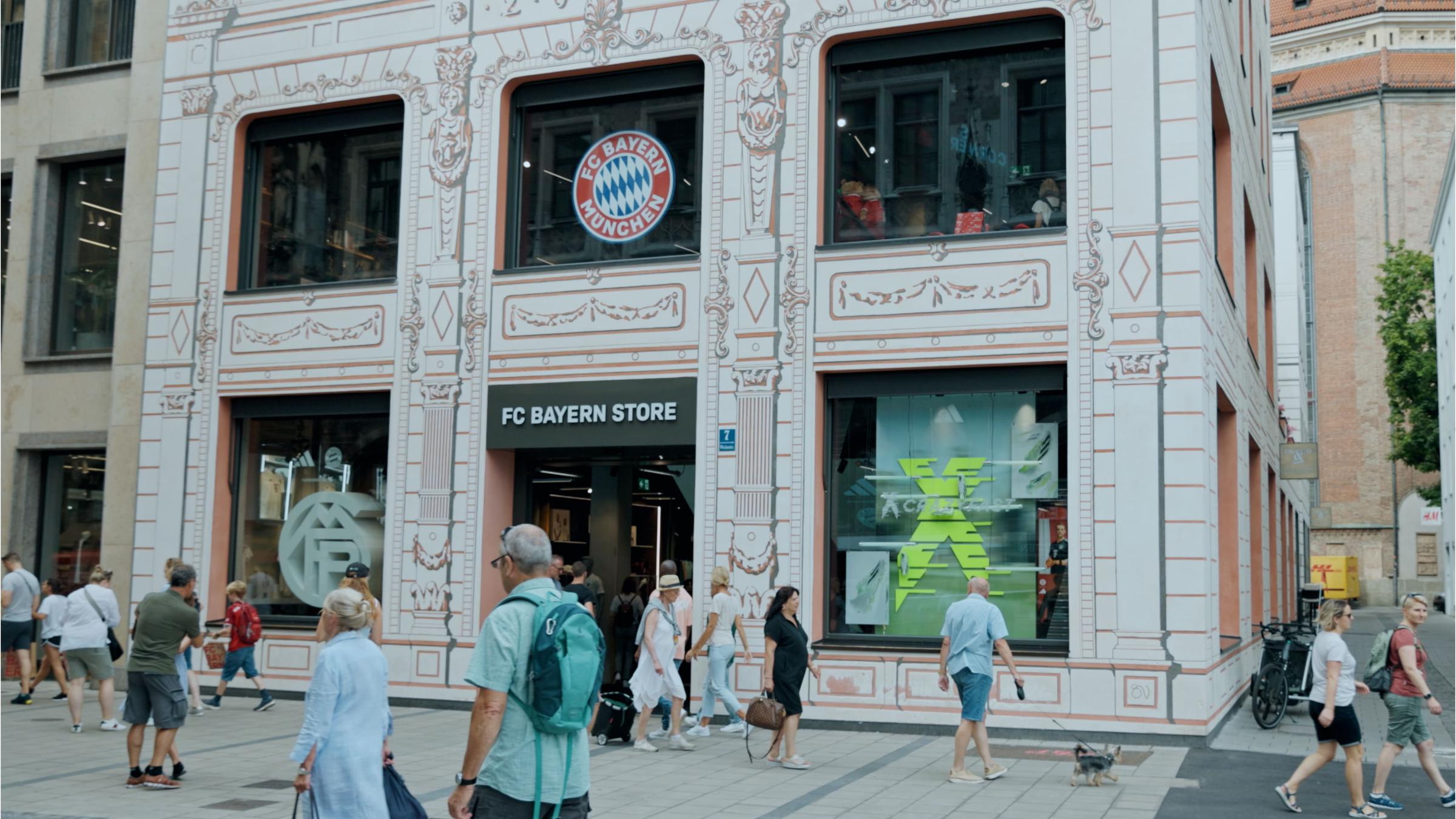 Pedestrians walking past the FC Bayern Munich store with logo visible.