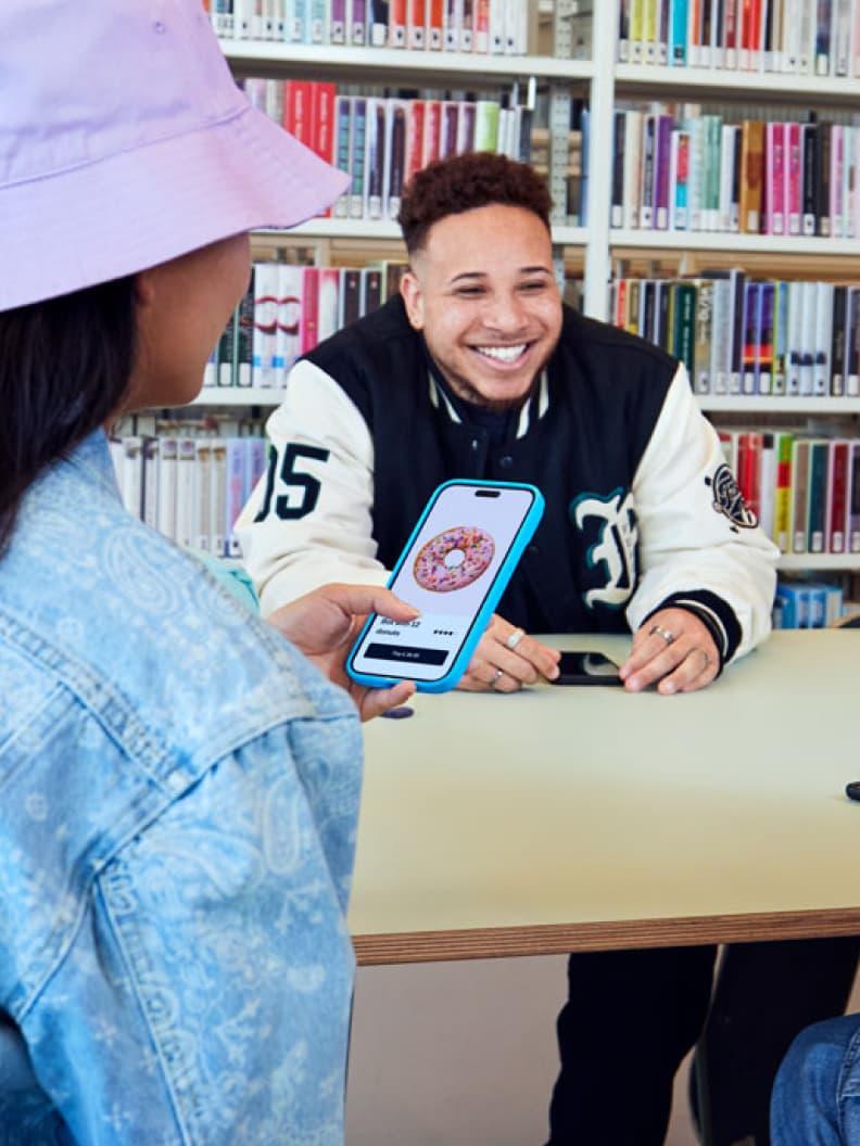 A smiling person presenting a mobile payment app to a customer in a library setting.