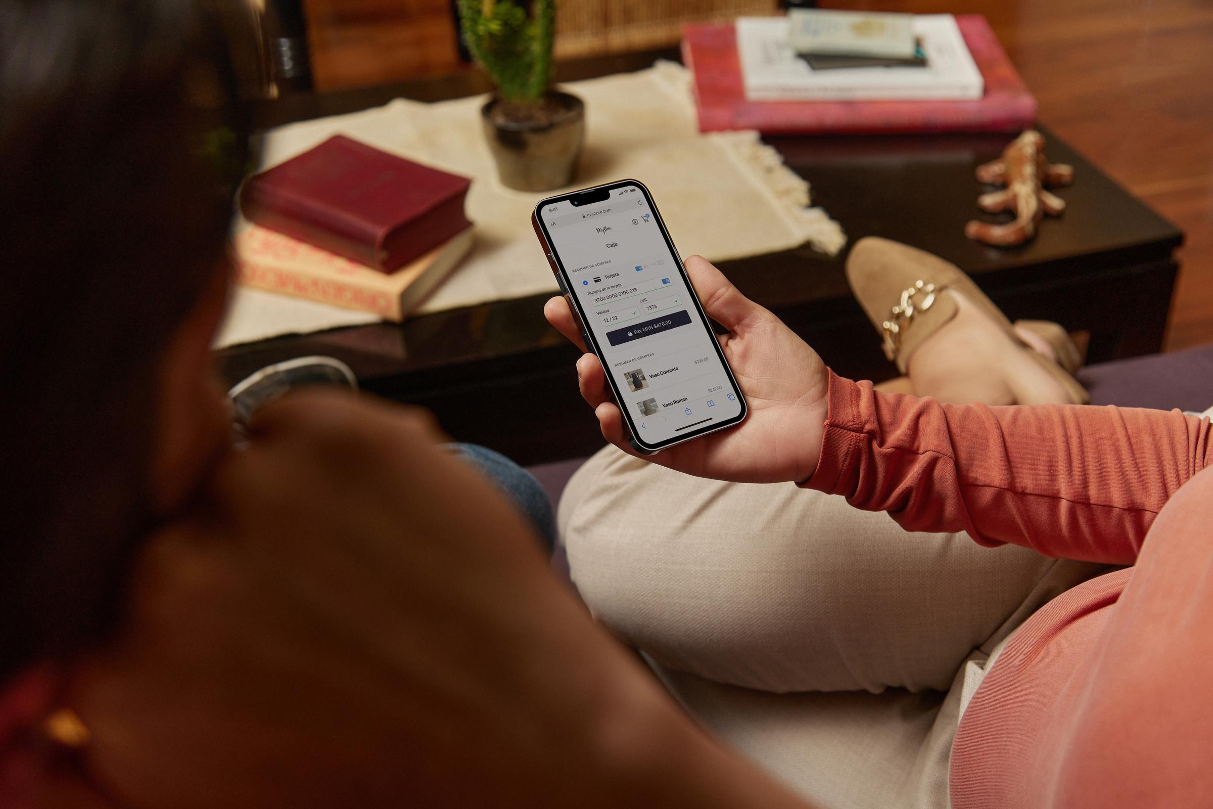 Personne assise sur un canapé en train d’utiliser l’application de paiement Adyen sur son smartphone.