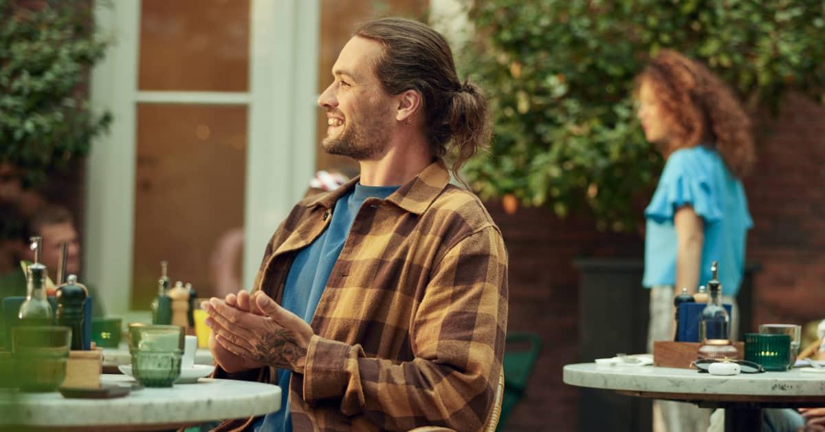 Mand der smiler og klapper i hænderne på en udendørs café.