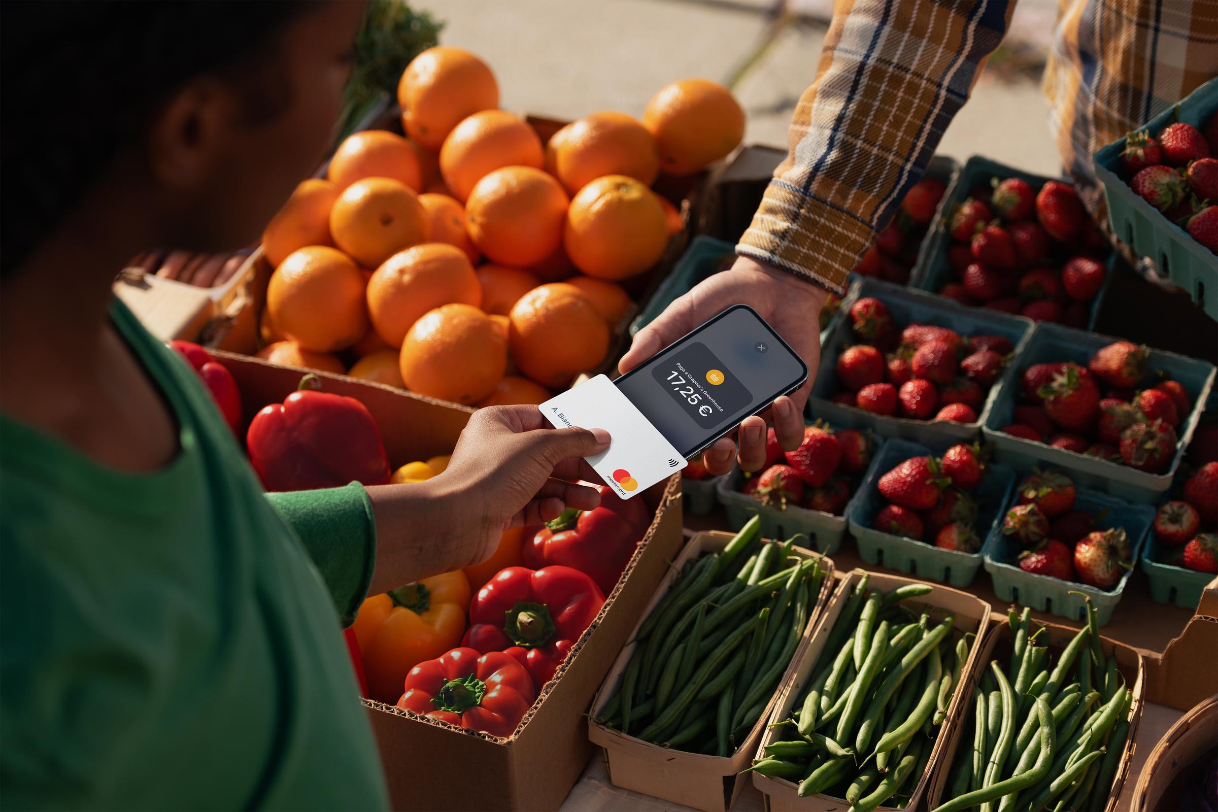 A customer at a vegetable stand in Italy tapping their iPhone at the seller's iPhone to pay for the purchase.