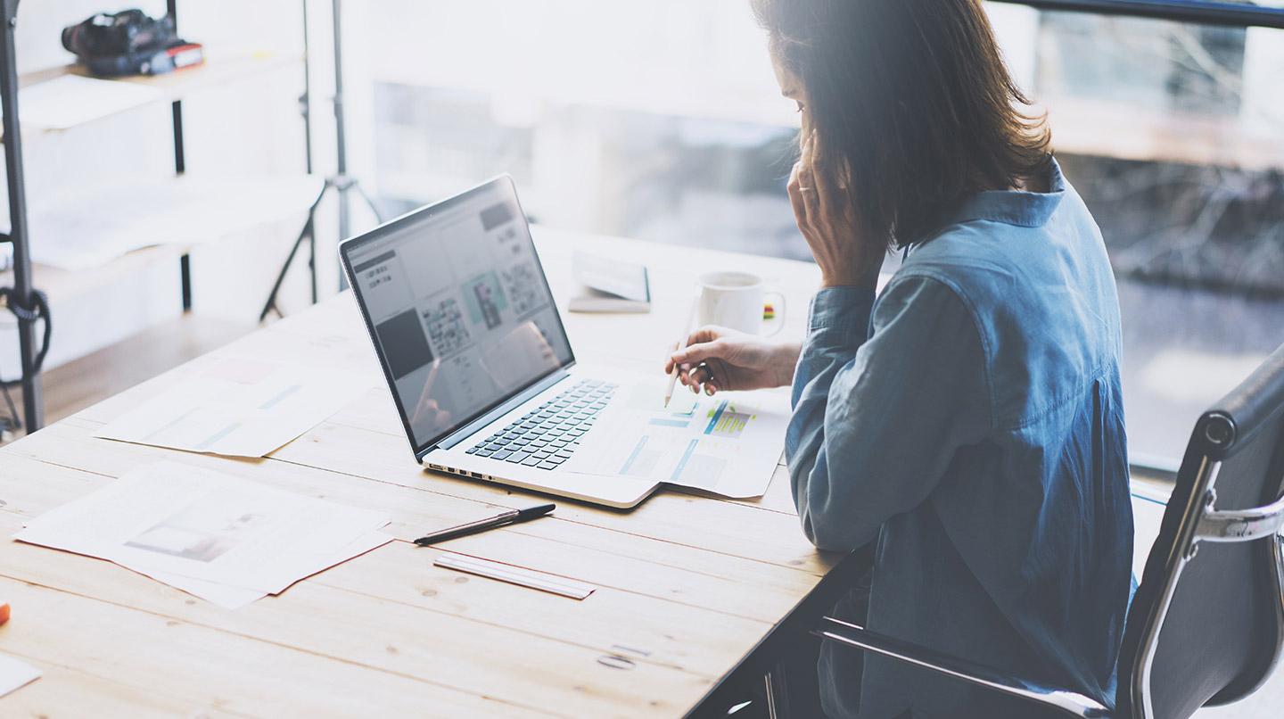Person working on a laptop at a desk with documents and a cup of coffee.