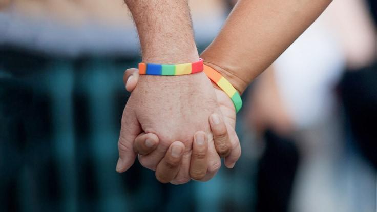 Two people holding hands with one wearing a rainbow bracelet.