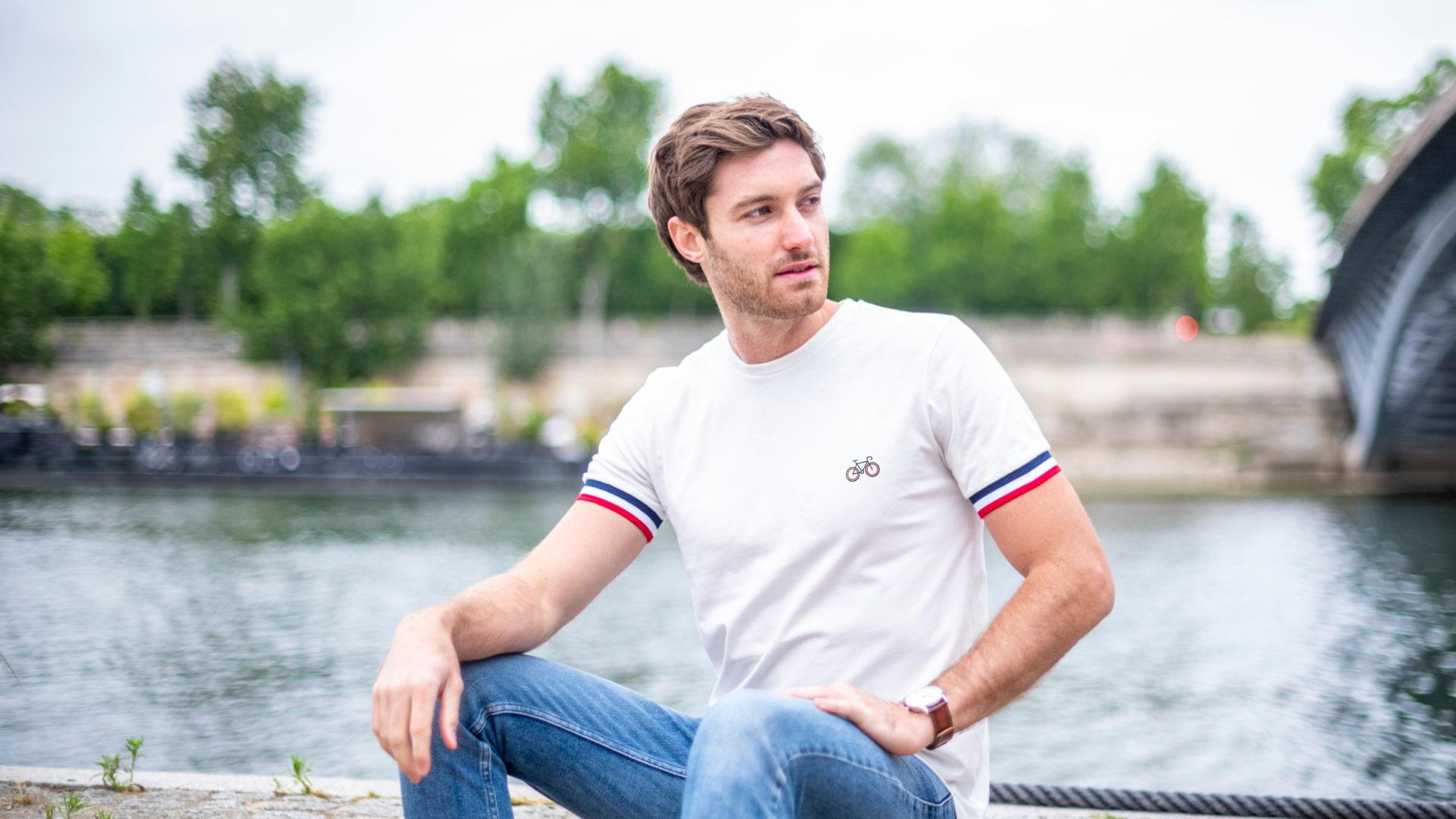 Homme assis au bord de l'eau avec une chemise blanche et un jean bleu.