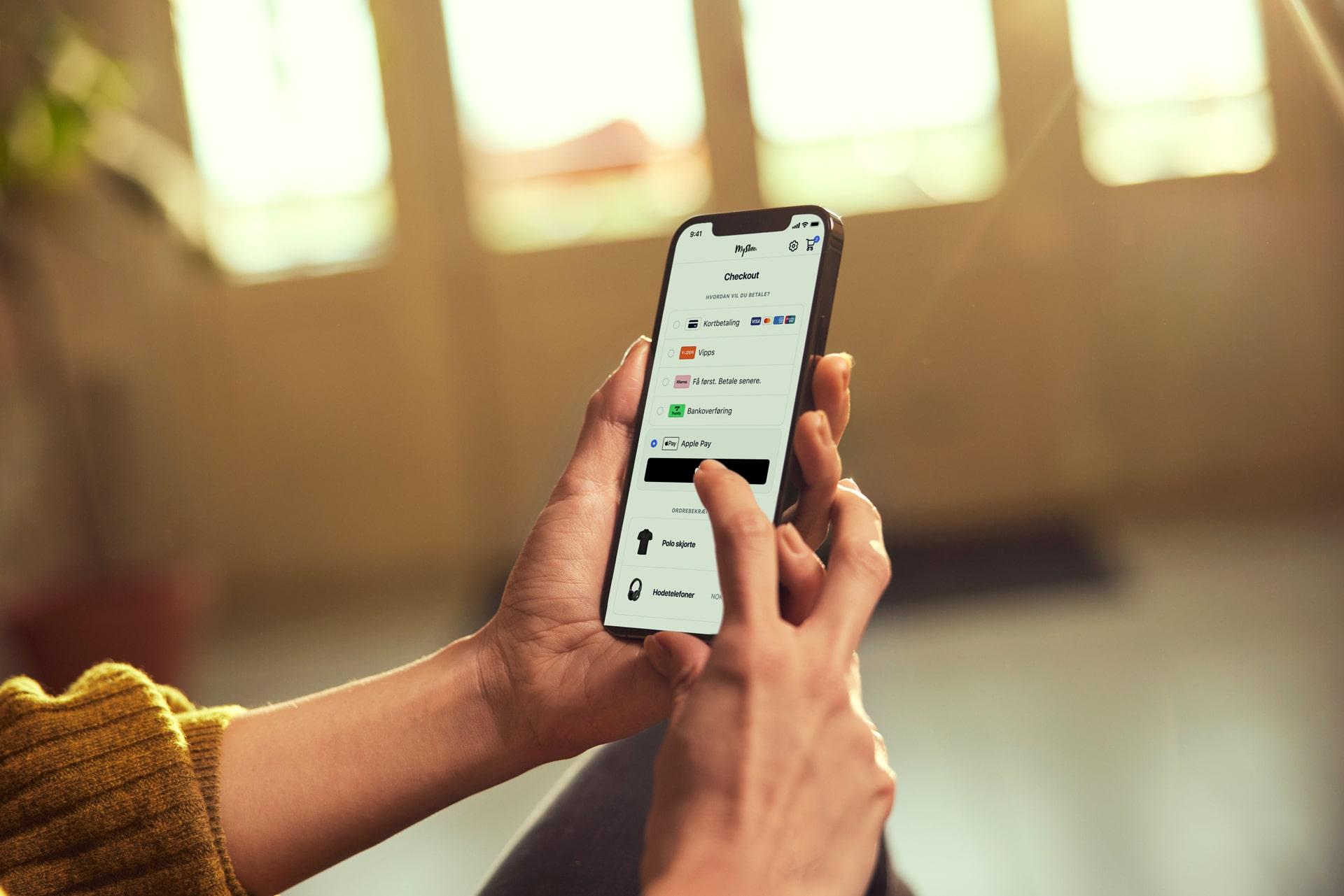 Nærbilde av hender som bruker en smarttelefon for å vise betalingsalternativer, inkludert Adyen-produkter.