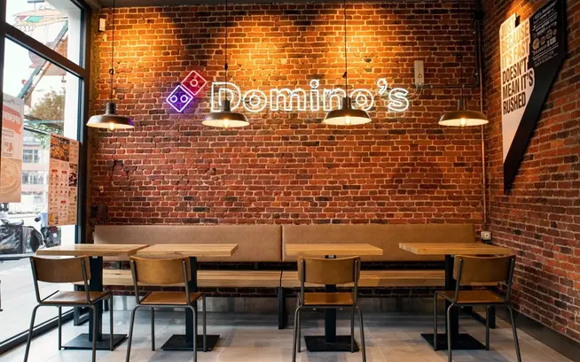 Interior of a Domino's Pizza restaurant with exposed brick walls and neon sign.