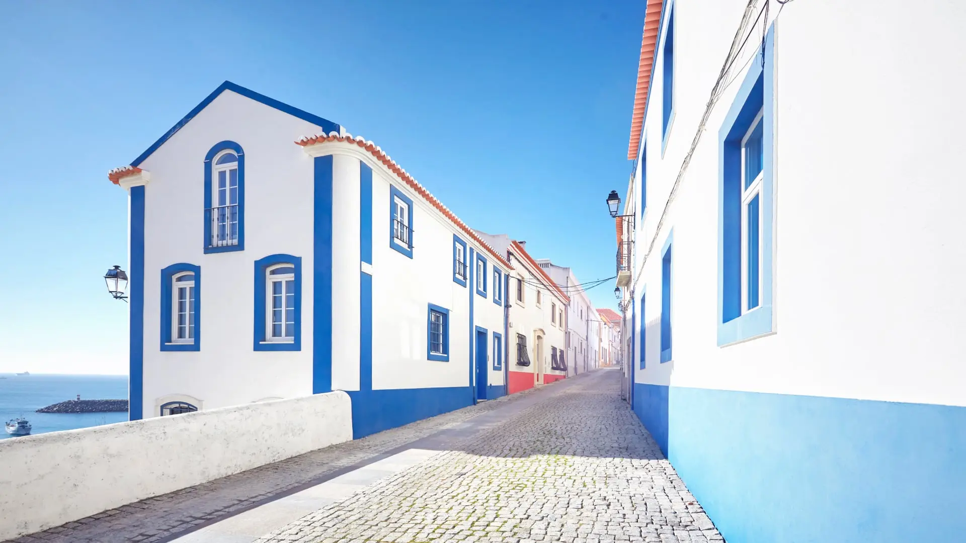 Bright sunny street with traditional Portuguese architecture, cobblestone pavement, and a glimpse of the sea.