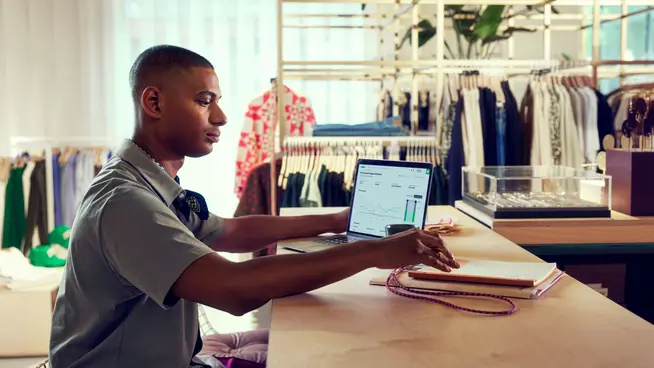 Hombre trabajando en una laptop con el panel de análisis de Adyen en pantalla en una tienda de moda minorista.