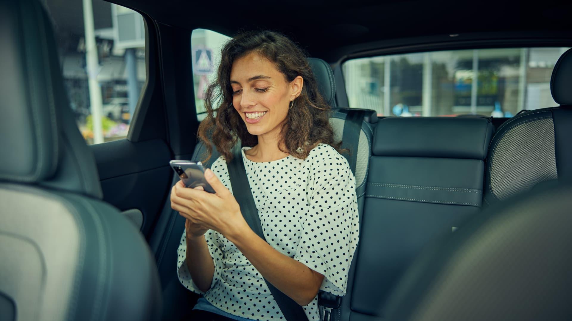 Smiling woman using smartphone while sitting in the backseat of a car.