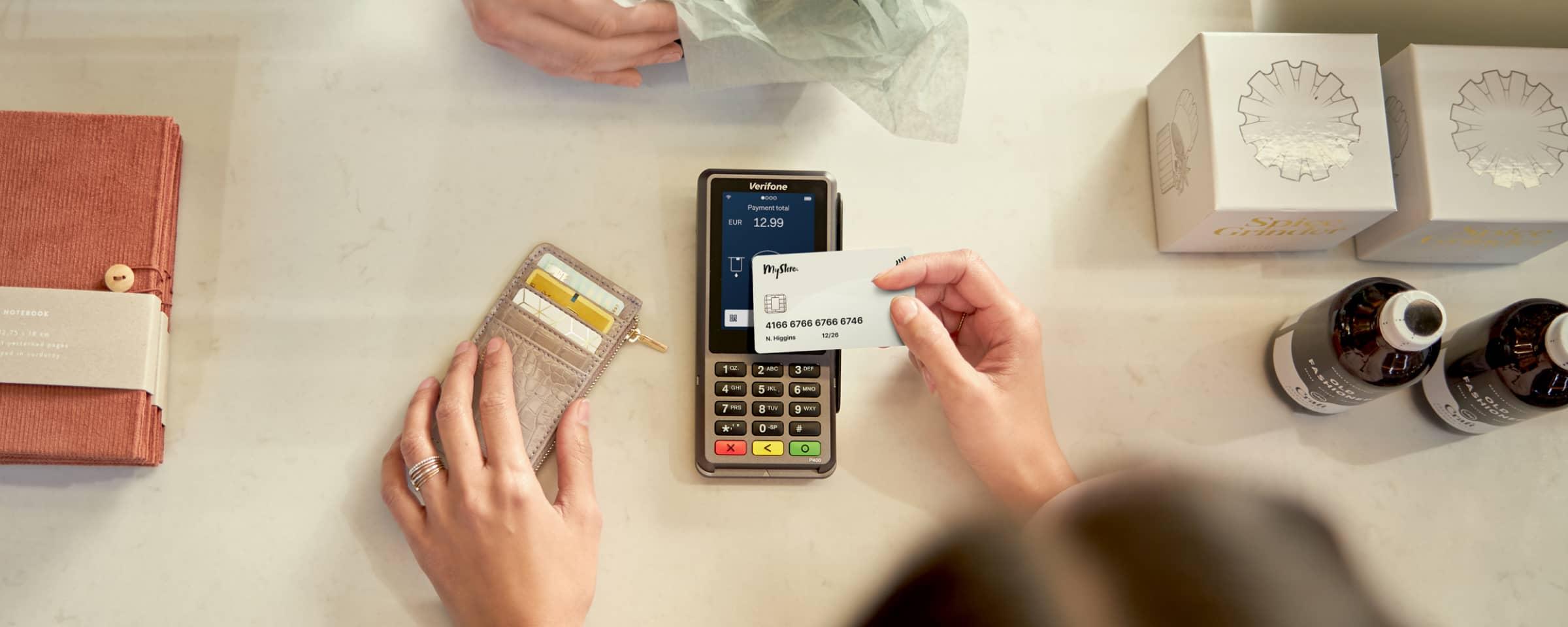 Pessoa usando um cartão em um terminal de pagamento Adyen ao lado de mercadorias variadas