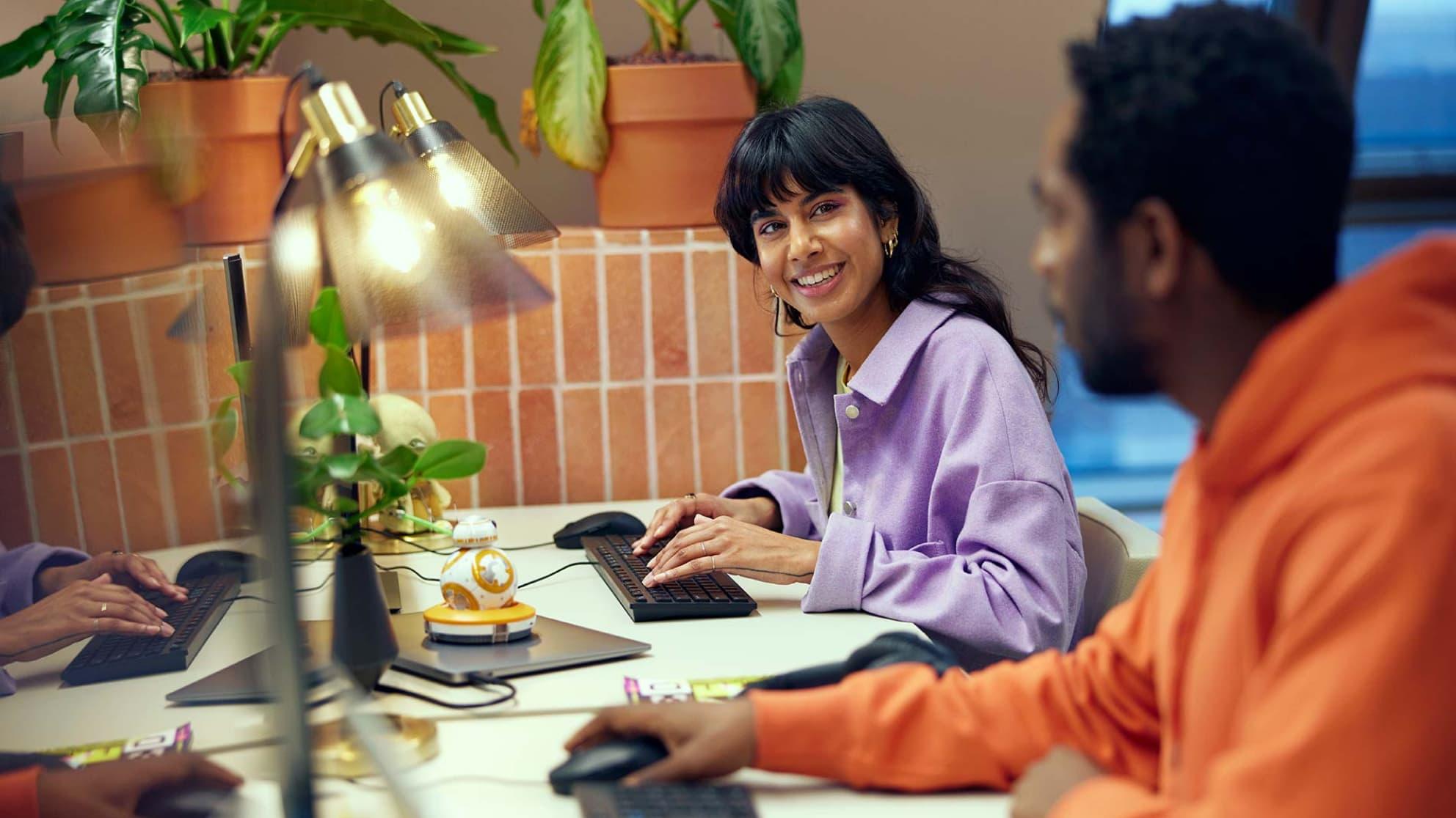 Two colleagues working at a desk with computers and a decorative desk lamp.