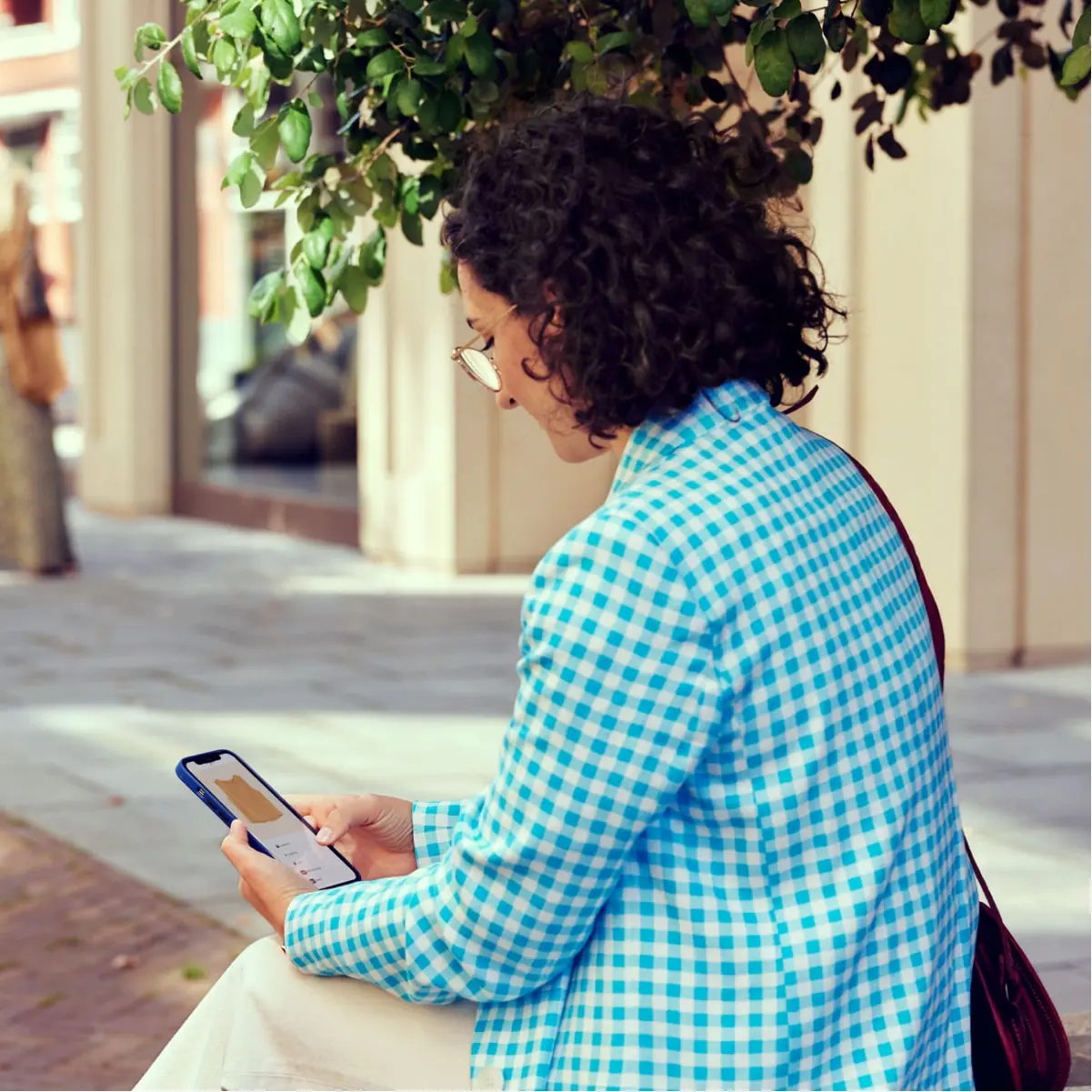 Person sitting outdoors using a smartphone to manage transactions.