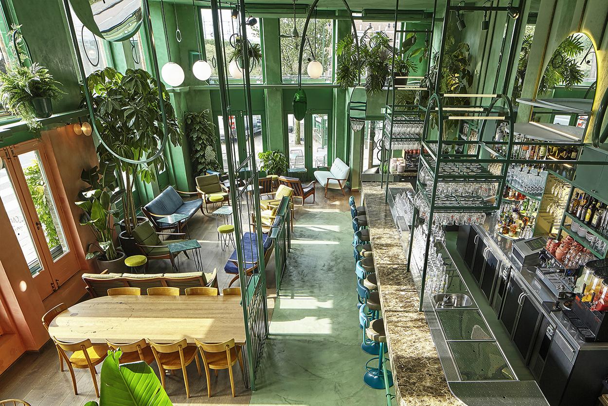 Lichte en luchtige café-interieur met groene muren, weelderige planten en een mengeling van moderne zitplaatsen en bar.
