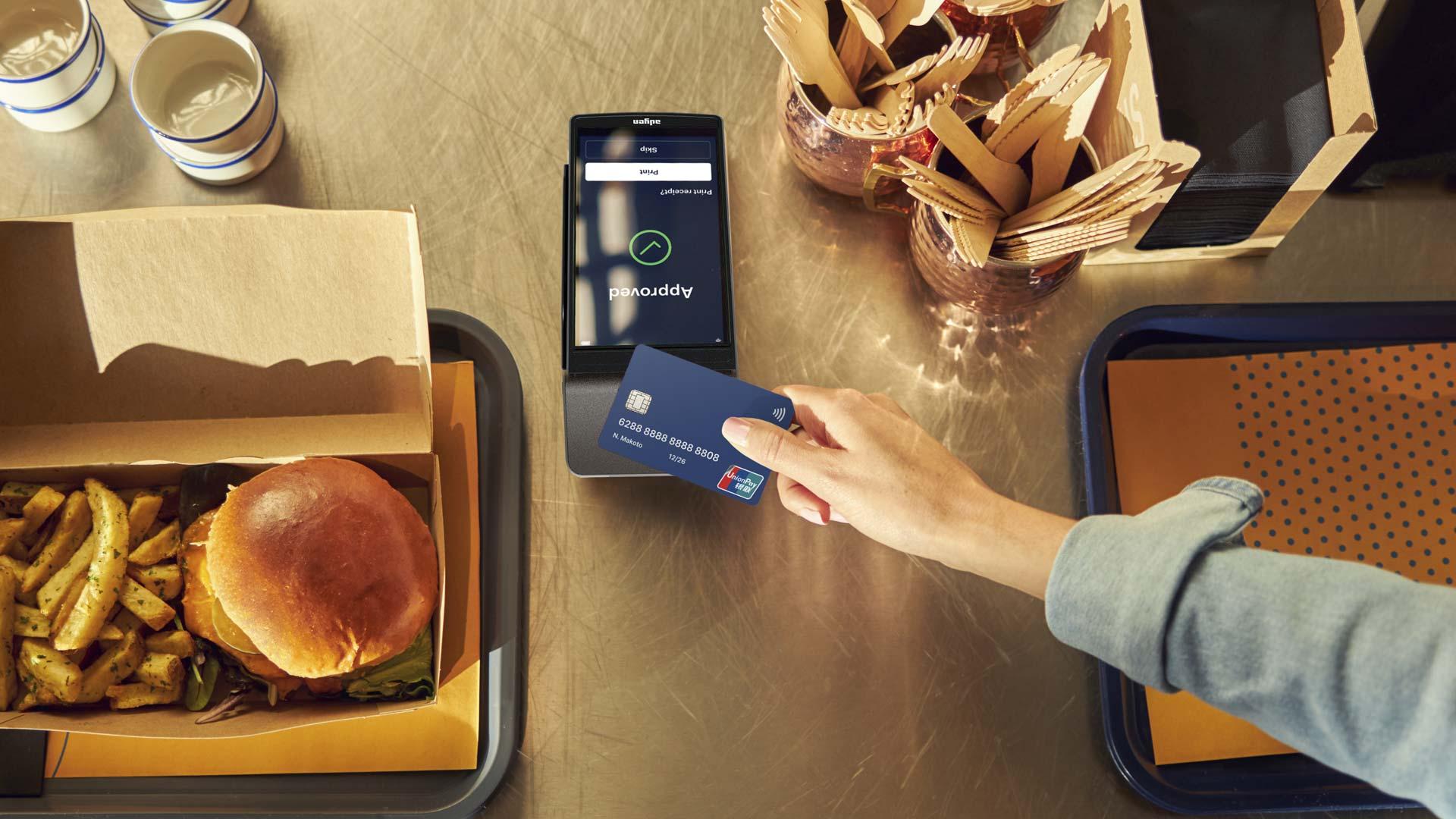 Person making a payment using a contactless UnionPay bank card on an Adyen terminal next to a fast food meal.