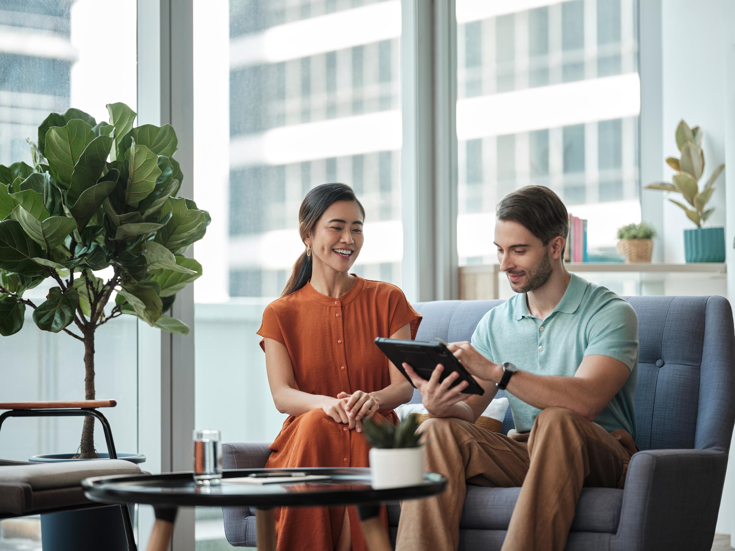 A man and woman sitting on a sofa while looking at an ipad