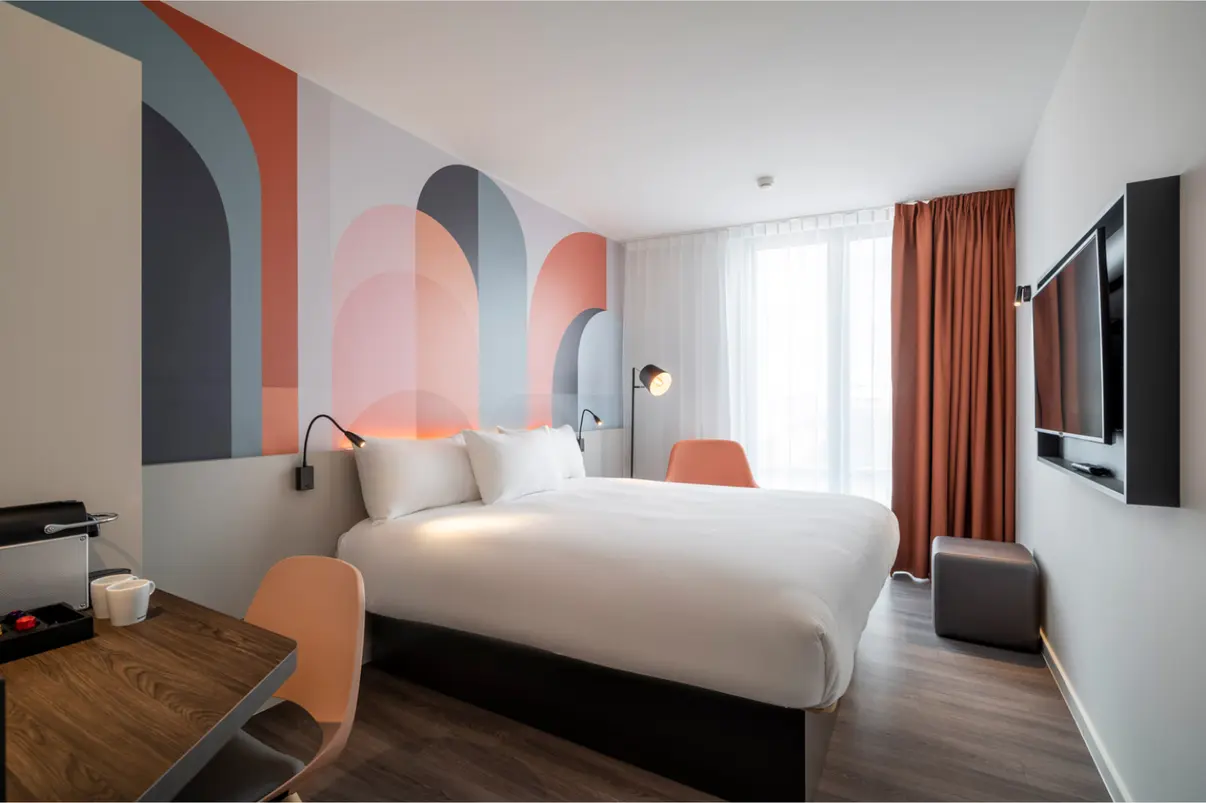 Quarto de hotel moderno com cama grande, padrão artístico na parede e móveis contemporâneos.