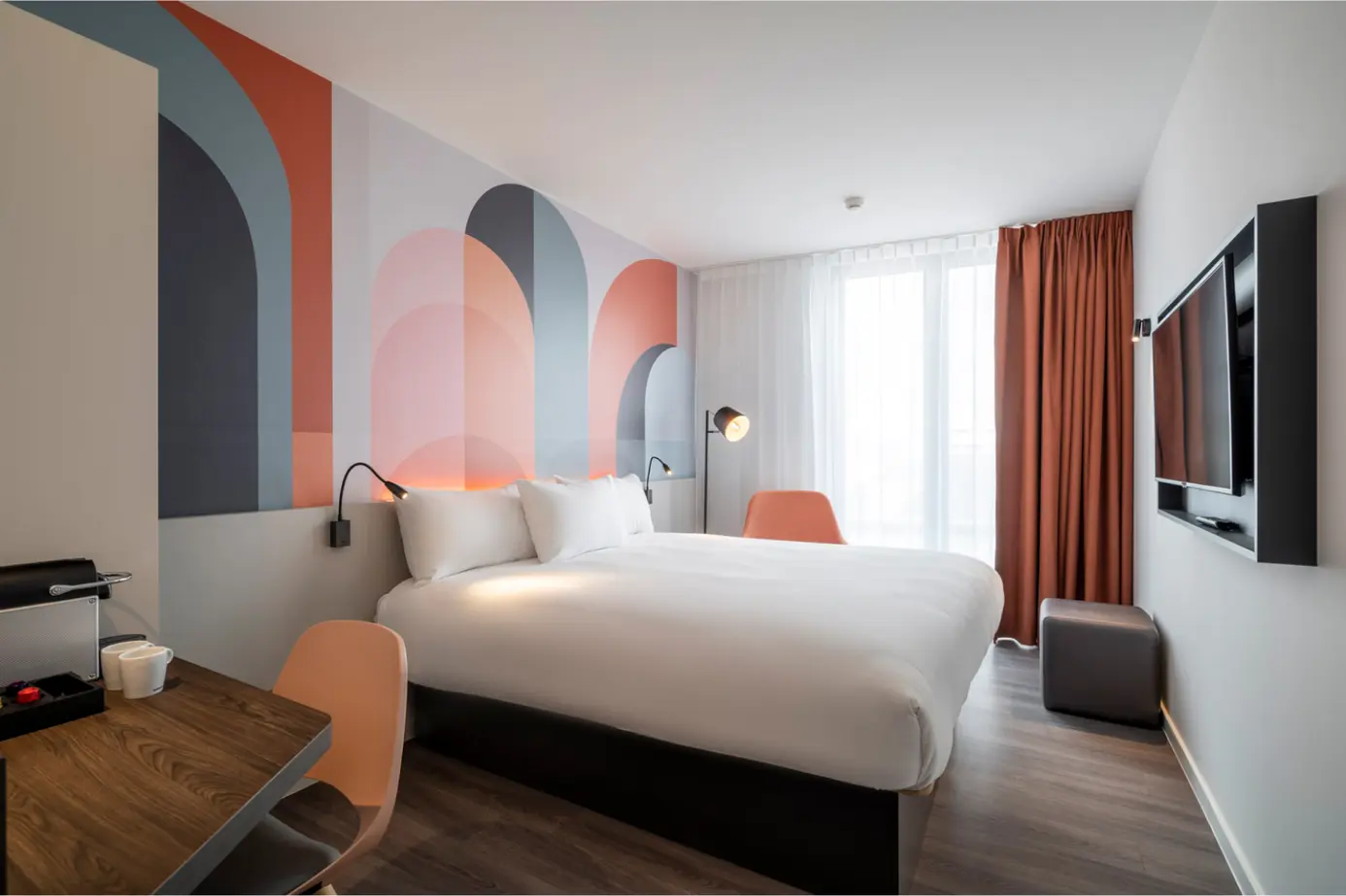 Quarto de hotel moderno com cama grande, padrão artístico na parede e móveis contemporâneos.