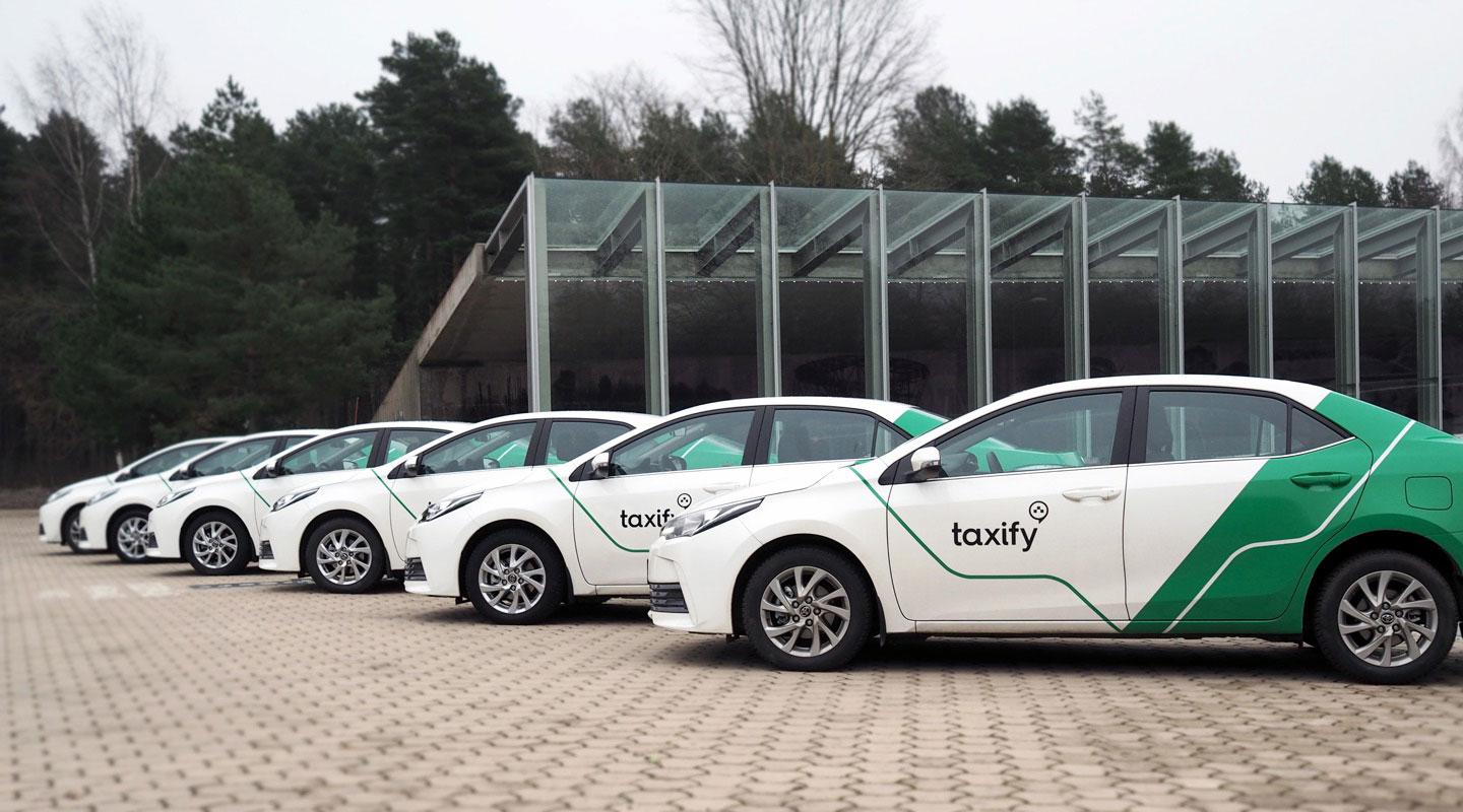 Row of white and green branded cars parked outside a modern building.