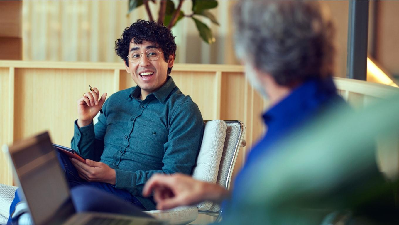 Dwie osoby prowadzące rozmowę, przy czym jedna trzyma pióro i uśmiecha się.