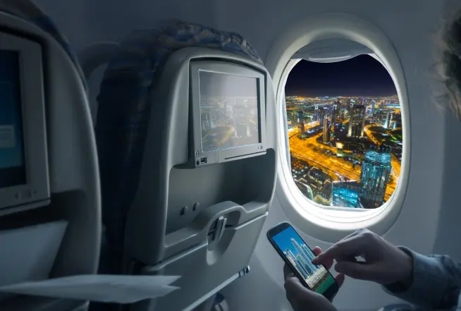 person holding phone while sitting in the airplane with view of dubai  from the window