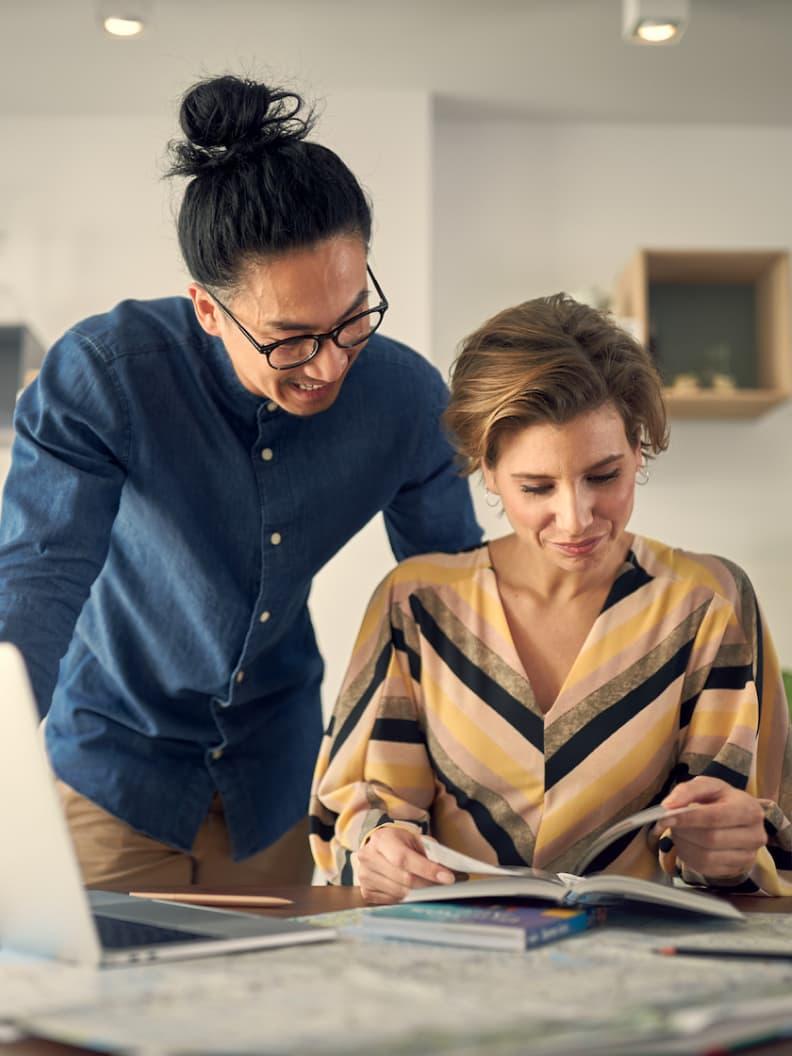 Two colleagues collaborating over documents on a desk with a laptop.