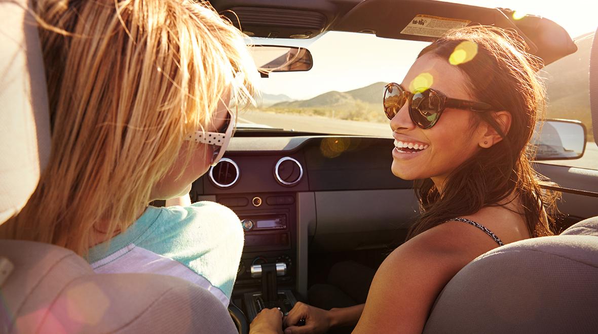 Two women smiling and enjoying a sunny car ride together.