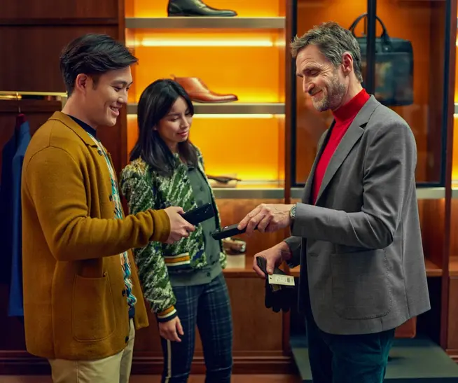 Man holding a card reader while another person pays with a smartphone in a store.