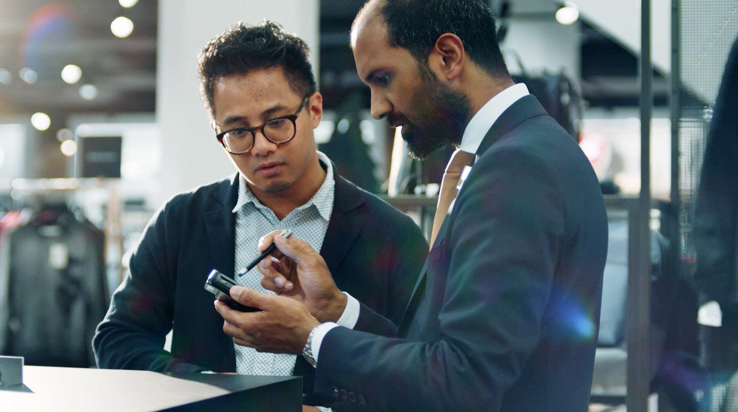 Two men, one holding a smartphone, examining Adyen's payment terminal.