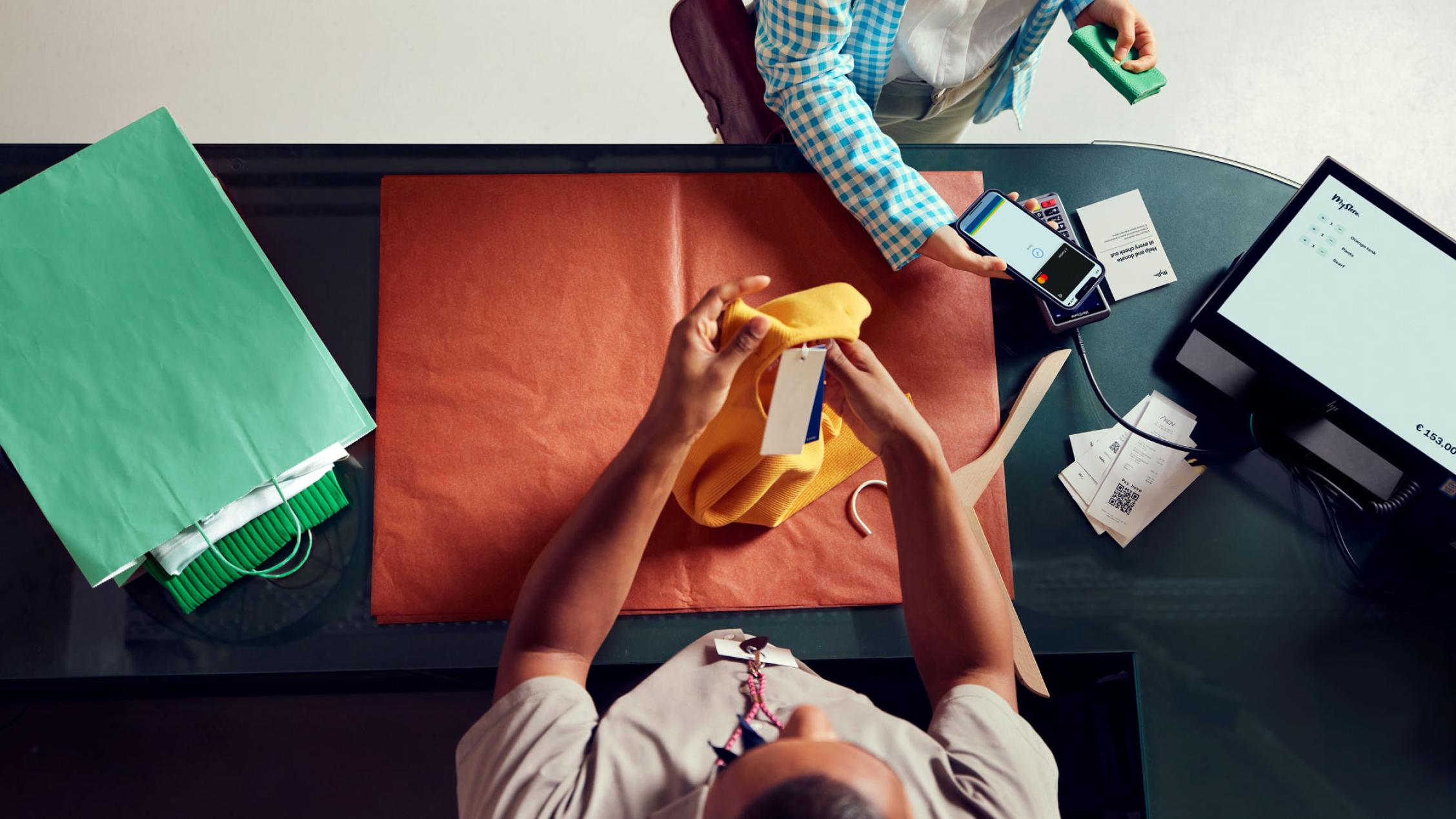 Kund använder en smartphone för en transaktion via Adyen POS-terminal vid en kassadisk med artiklar