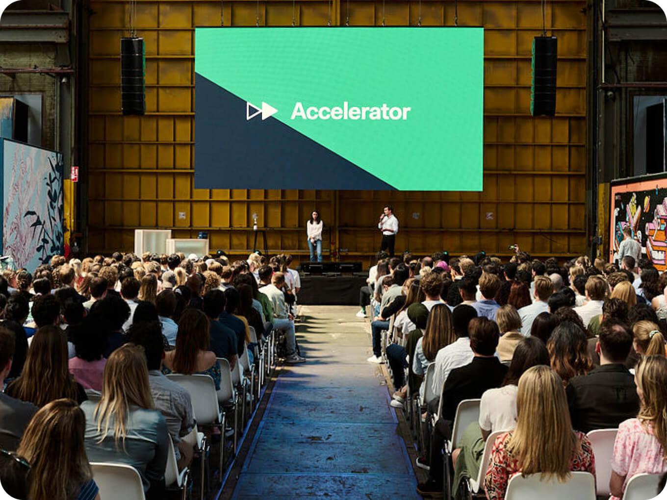 Público ouvindo uma apresentação em um evento de acelerador em um local grande