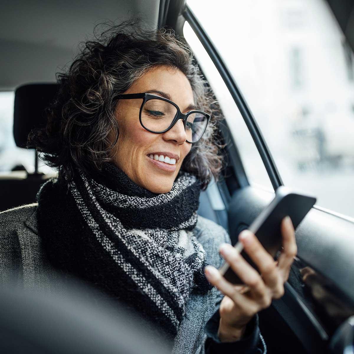 Mujer sonriendo con gafas usando un smartphone en el coche.