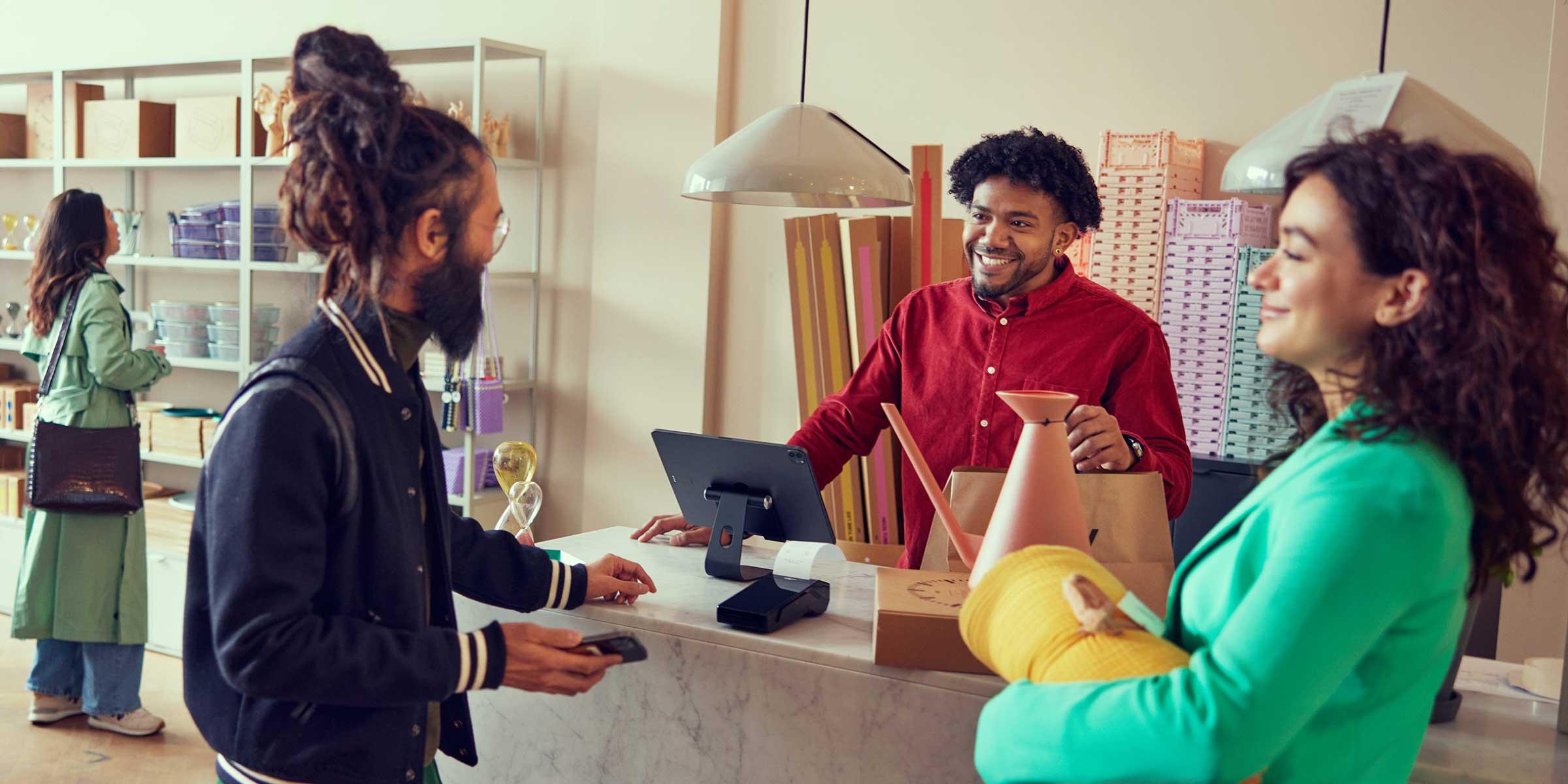 Kassamedewerker lacht naar een klant die met een smartphone betaalt bij een winkelkassa.
