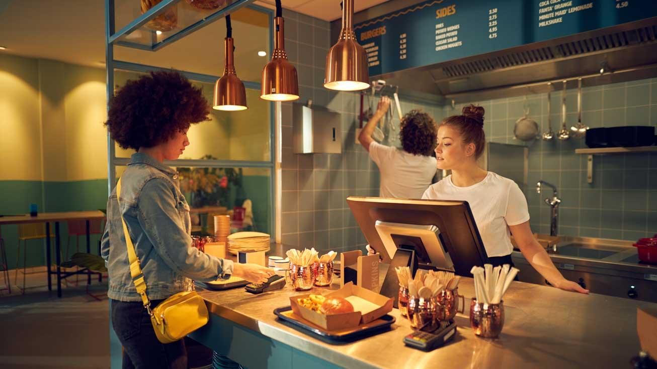Cliente pagando com um smartphone no caixa de um restaurante com funcionário assistindo.