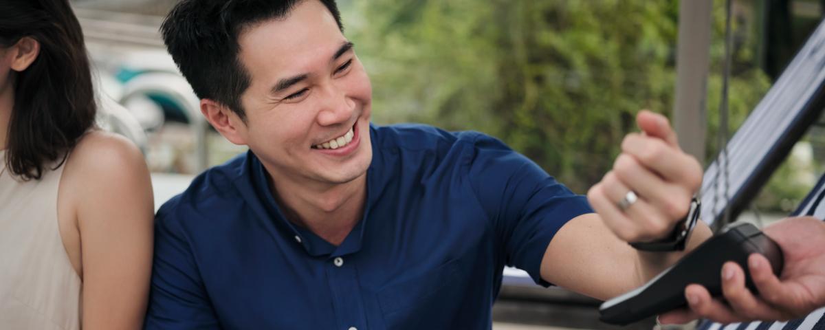 Man in blue shirt smiling while making a payment with a card reader.