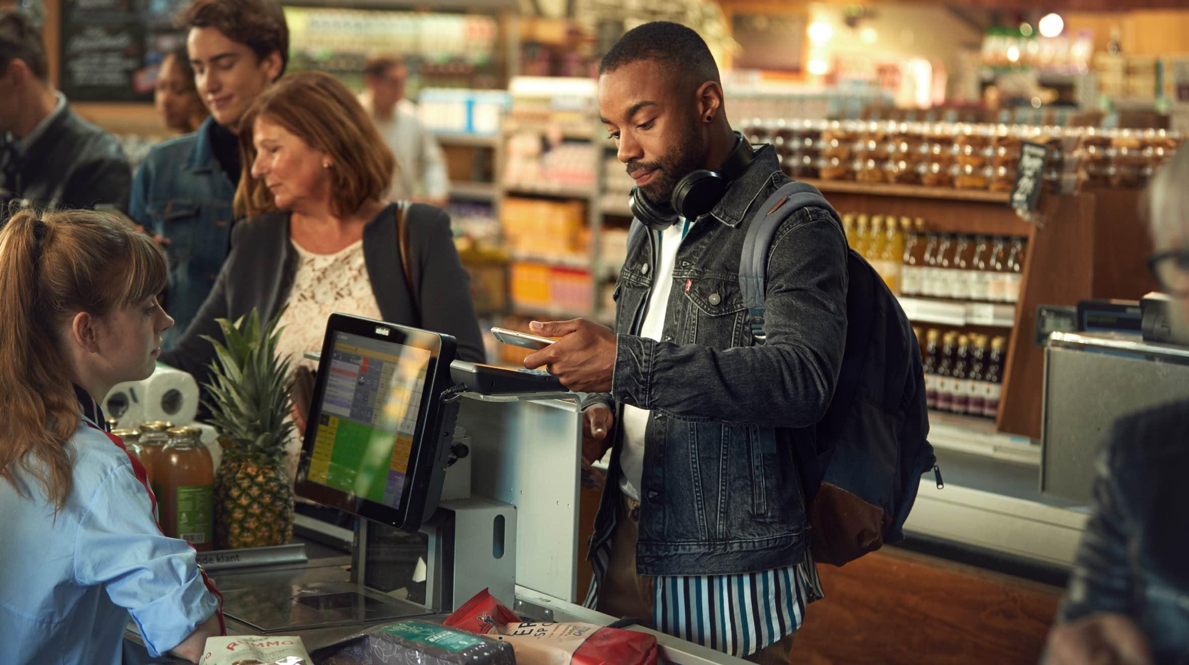 Mann verwendet Smartphone, um eine Zahlung an einem Adyen-Kassen-Terminal in einem Supermarkt durchzuführen.