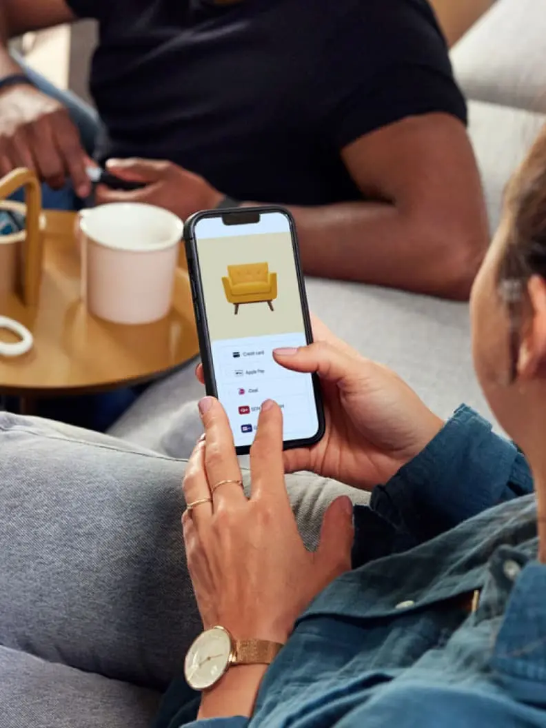 Detailní pohled na osobu držící smartphone se zobrazením nákupního košíku s židlí a platebními možnostmi.