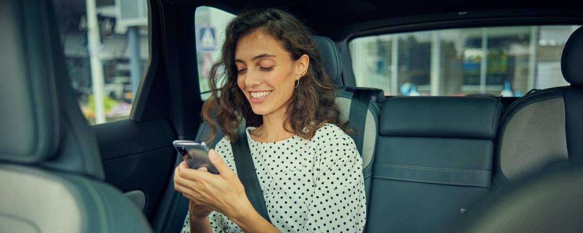Smiling woman using a smartphone in the backseat of a car.